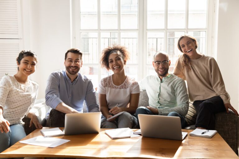The photograph captures a group of young female and male friends of diverse ethnic backgrounds sitting happily together.